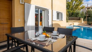 A dining area with a table set for two, a pool, and a door with shutters. - Holiday Home “Villa Can Gaya” with Pool, Terrace & Wi-Fi (Alcudia)