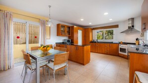 A modern kitchen with wooden cabinets, a central island, and a dining area with wicker chairs. - Holiday Home “Villa Can Gaya” with Pool, Terrace & Wi-Fi (Alcudia)