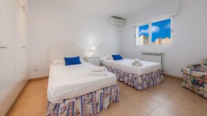 A room with two beds, a radiator, a window with a city view, and a floral sofa. - Holiday Home “Villa Can Gaya” with Pool, Terrace & Wi-Fi (Alcudia)