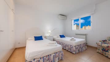 Una habitación con dos camas, un radiador, un ventanal con vistas a la ciudad y un sofá con motivos florales.