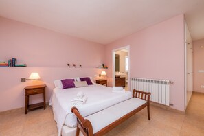 A bedroom with a bed, bedside tables, a radiator, and a bathroom visible through an open door.