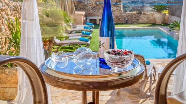 A table with a bottle of wine, glasses, and a bowl of fruit by a poolside. - Casa del Sol with Sea View, Wi-Fi, Pool, Balcony & Terrace; Street Parking (Búger)