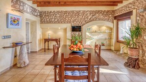A dining area with a wooden table, chairs, a bowl of fruit, and a stone wall. - Casa del Sol with Sea View, Wi-Fi, Pool, Balcony & Terrace; Street Parking (Búger)