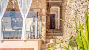 A stone-walled room with a glass table and chairs, a wooden bench, and a staircase leading to an upper level. - Casa del Sol with Sea View, Wi-Fi, Pool, Balcony & Terrace; Street Parking (Búger)