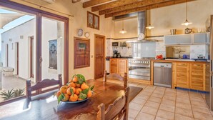 A kitchen with wooden cabinets, a dining table with a bowl of oranges, a stove, and a dishwasher. - Casa del Sol with Sea View, Wi-Fi, Pool, Balcony & Terrace; Street Parking (Búger)