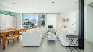 Un salon moderne avec un coin repas, des meubles blancs, un téléviseur et une vue sur la ville.
