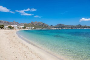 A beach with clear turquoise water, a sandy shore, and buildings in the background. - Apartment Can Fiol II near the Beach with Sea View, Wi-Fi & Terrace (Port De Pollença)