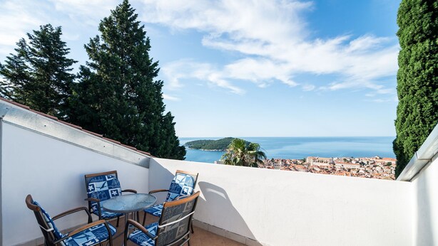 A terrace with a table and chairs, overlooking a coastal town and the sea. - Apartment Srđ  (Dubrovnik)