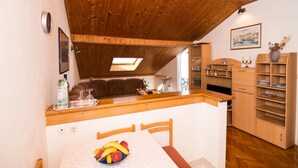 A compact kitchen with wooden ceiling beams, a dining area with a table and chairs, and a small seating area with a sofa. - Apartment Srđ  (Dubrovnik)