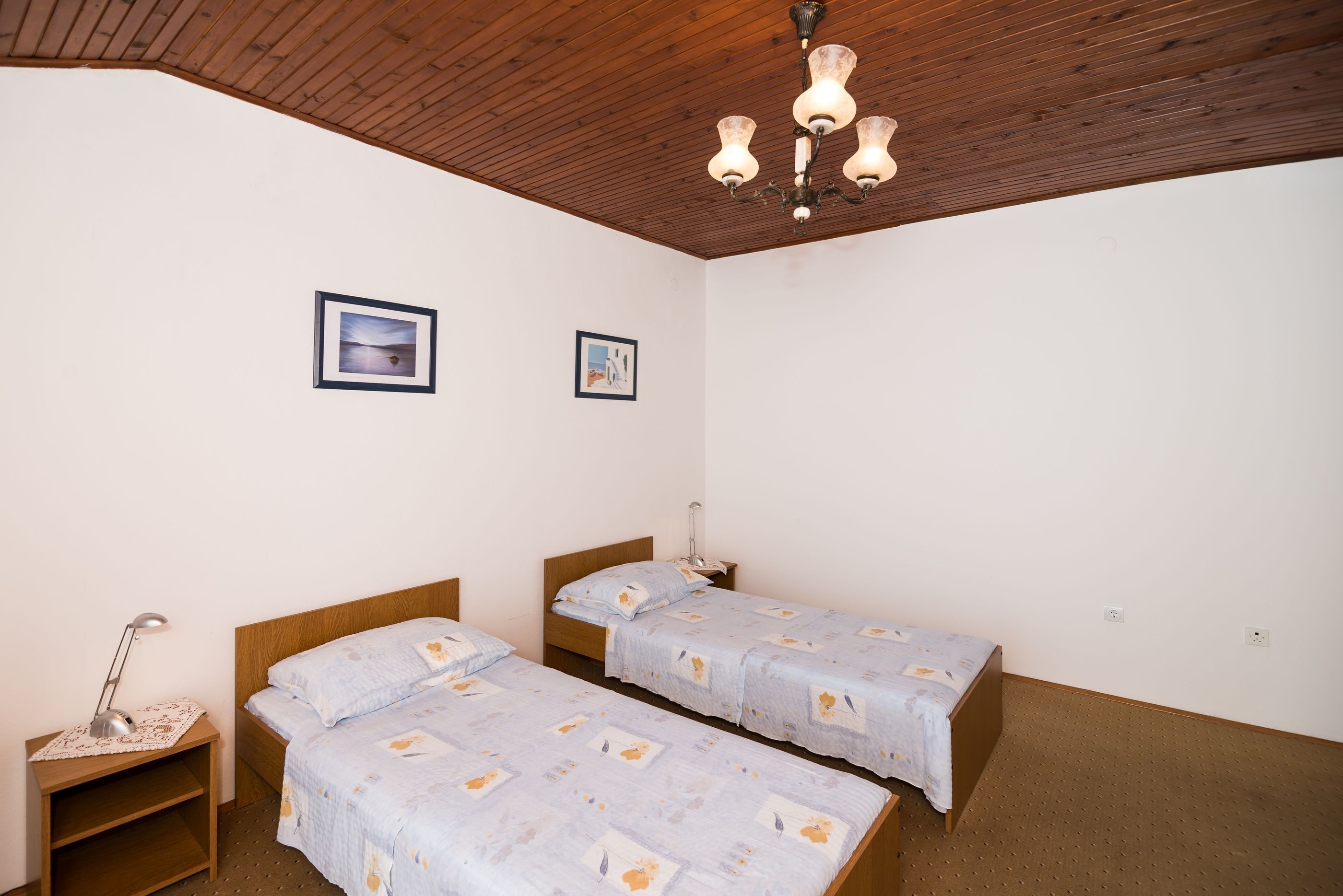 A bedroom with two single beds, wooden headboards, a wooden ceiling, and a hanging light fixture.