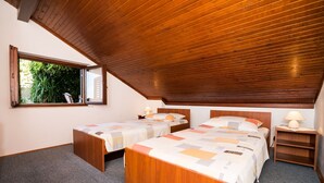 A bedroom with two beds, wooden ceiling, and a window with a view of greenery. - Apartment Srđ  (Dubrovnik)