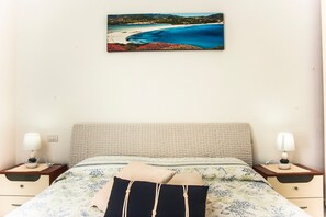 A bed with a floral bedspread, two bedside tables with lamps, and a painting of a beach scene on the wall.