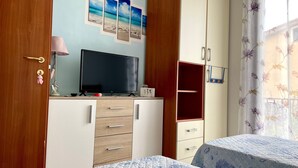A bedroom with a TV, wooden cabinets, a bed with a floral bedspread, and a window with floral curtains. - Holiday Apartment ‘Casa Vacanze Pula' with Balcony & Terrace (Pula)