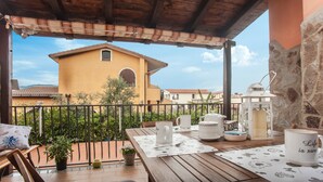 A wooden balcony with a table set for two, a potted plant, and a view of a yellow building with a red roof. - Holiday Apartment ‘Casa Vacanze Pula' with Balcony & Terrace (Pula)
