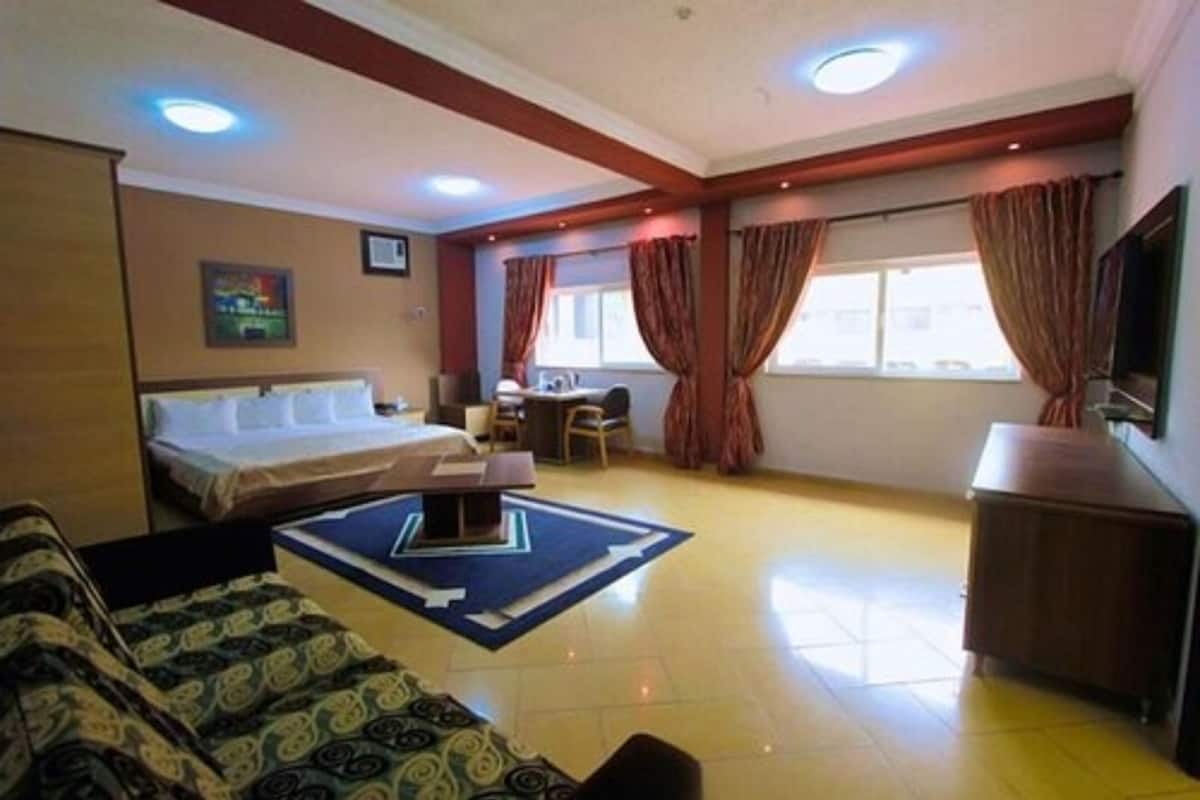 A hotel room with a bed, a desk, a chair, a TV, and a sofa.