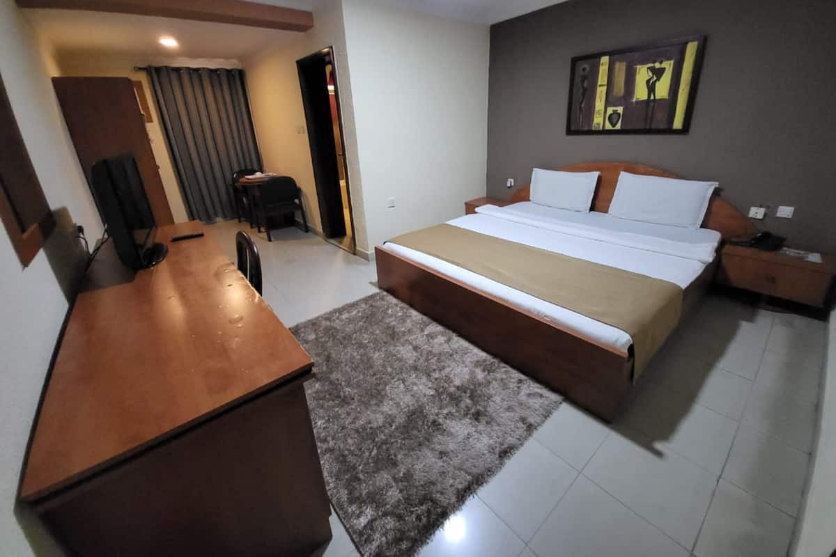 A hotel room with a large bed, a wooden desk, a chair, a TV, and a painting on the wall.