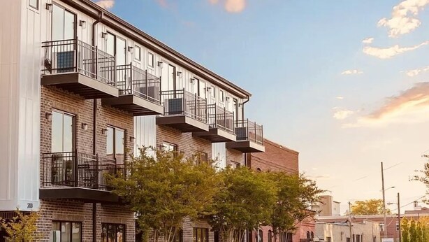 Un immeuble à plusieurs étages doté de balcons et d’une façade en briques, avec un ciel dégagé.