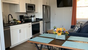 Une cuisine moderne avec des meubles blancs, des appareils en acier inoxydable et un coin repas comprenant une table et des bancs en bois.