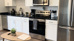 Une cuisine moderne avec des armoires blanches, des appareils en acier inoxydable, un four à micro-ondes, une machine à café et un réfrigérateur.