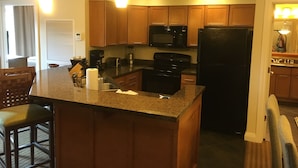 A compact kitchen with wooden cabinets, a black refrigerator, a microwave, and a coffee maker. There are two bar stools and a small island with a sink. - Wyndham Great Smokies Lodge at Wilderness water park(s) included (Sevierville)