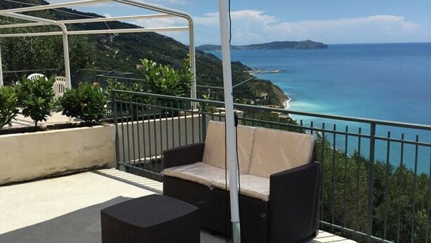 A balcony with a wicker sofa and a small table, overlooking a coastal view with clear blue waters and distant islands. - Residenze Cutrì Holiday Home Cilento Bilo 2 (Pisciotta)