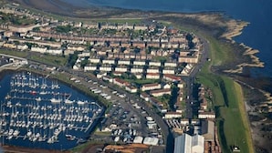 An aerial view of a coastal town with a marina filled with boats, residential buildings, and a prominent building with a sign. - Marina View, Lovely Upper 3 Bedroom Apartment (Troon)