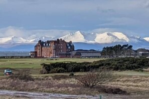 A large, historic building with a symmetrical facade and a prominent central tower, surrounded by a well-maintained lawn and a distant mountain range. - Marina View, Lovely Upper 3 Bedroom Apartment (Troon)