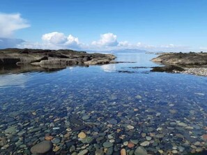A clear view of a pebble beach with calm water and distant mountains. - Marina View, Lovely Upper 3 Bedroom Apartment (Troon)