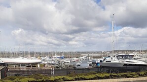 A marina with various boats docked, a clear sky, and a distant view of land. - Marina View, Lovely Upper 3 Bedroom Apartment (Troon)