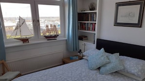 A bedroom with a bed, a bookshelf, a framed picture, and a window with a sailboat model. - Marina View, Lovely Upper 3 Bedroom Apartment (Troon)