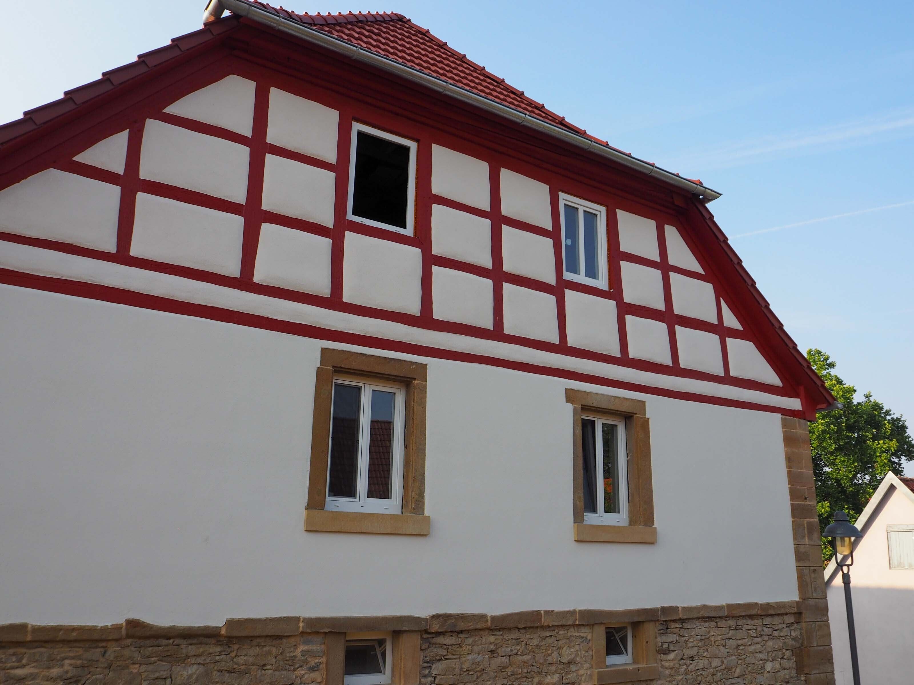 Ett traditionellt hus med korsvirkeskonstruktion, rött tak, vita väggar och en grund av sten.
