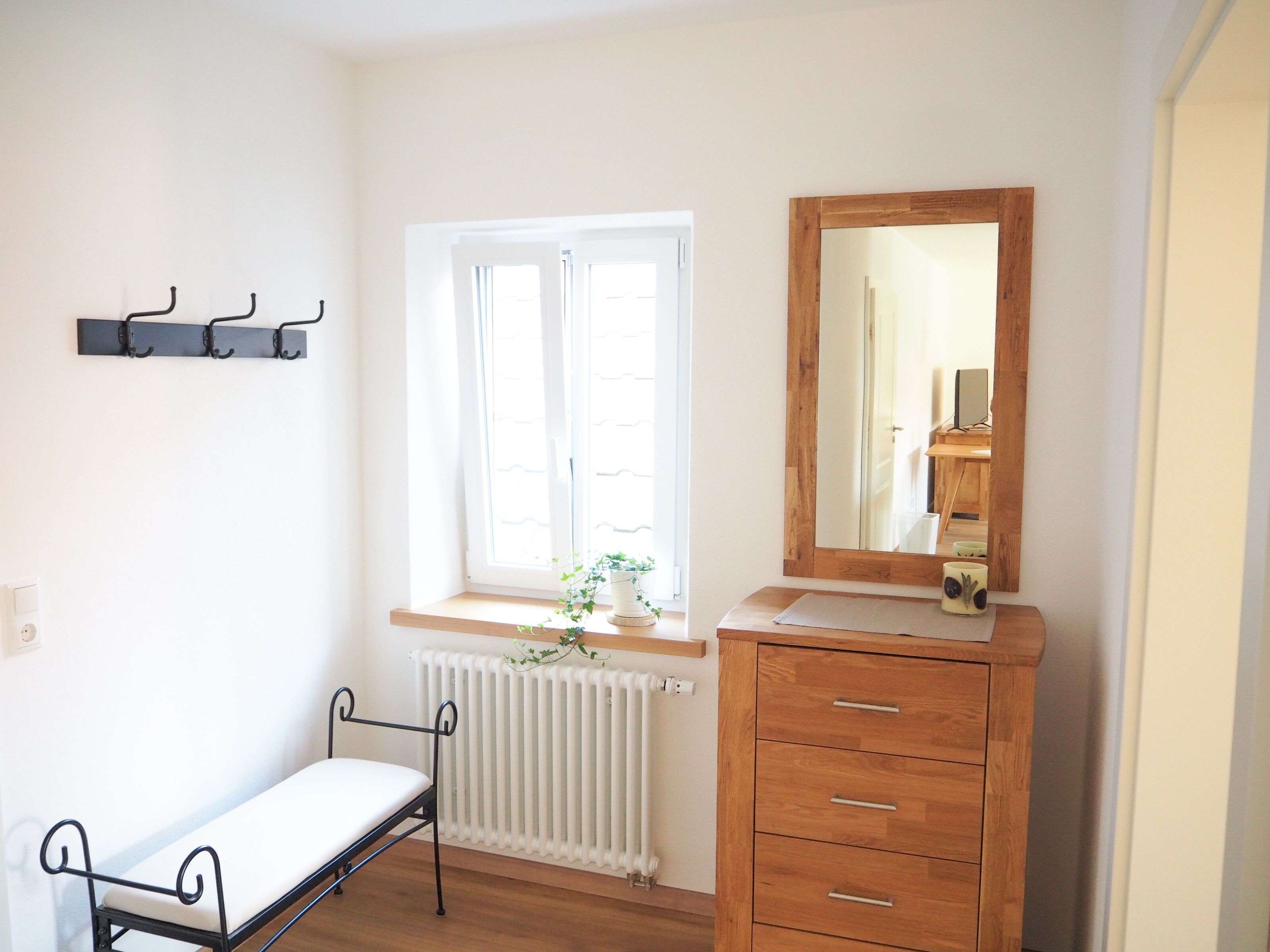 Ein Schlafzimmer mit Bett, Schminktisch, Spiegel, Heizkörper und einem Fenster mit Vorhängen.