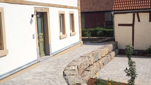 Ein Gebäude mit einem Kiesweg, der zu einer grünen Tür führt, ein kleiner Garten mit Pflanzen und ein Ziegeldach.
