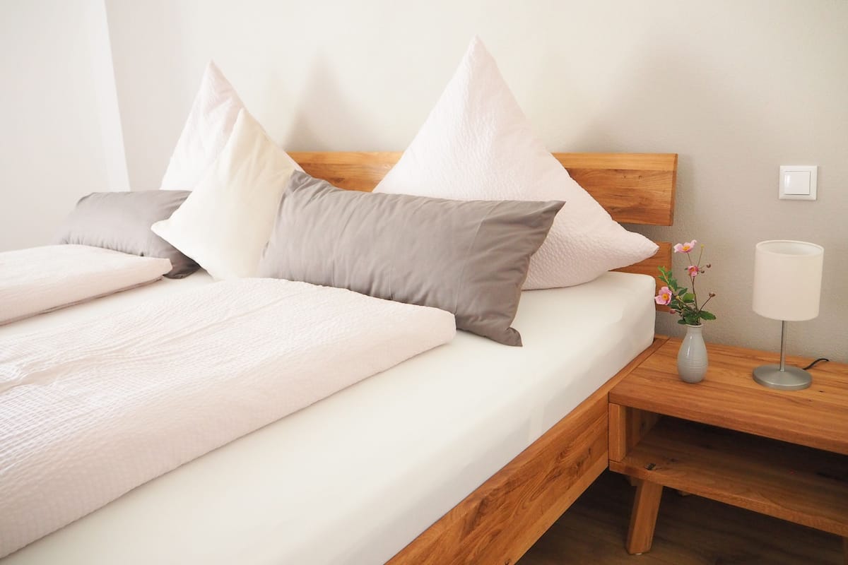 A neatly made bed with a wooden headboard, a bedside table with a lamp, and a small vase with flowers.