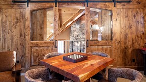 Un interior de madera con una gran mesa y sillas, un tablero de ajedrez y una pared de piedra.