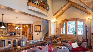 Amplia sala de estar con una escalera de madera, una chimenea acogedora y un gran ventanal con vistas a un bosque.