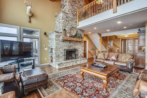 A spacious living room with a stone fireplace, leather furniture, and a large TV.
