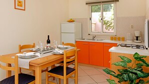 A compact kitchen with orange cabinets, a white refrigerator, and a window with a view of greenery. - HOUSE  DRAGOJEVIC (Vela Luka)