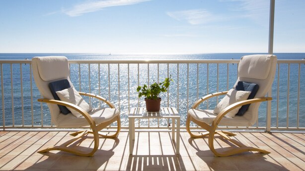 A balcony with two rocking chairs and a small table with a potted plant, overlooking a body of water. - A28 EDIFICIO RIO 4º 14 (Calpe)