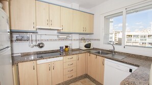 A compact kitchen with wooden cabinets, a built-in microwave, and a window providing a view of the city. - A28 EDIFICIO RIO 4º 14 (Calpe)