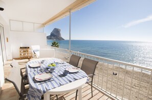 A balcony with a table set for dining, overlooking a beach and a rocky outcrop. - A28 EDIFICIO RIO 4º 14 (Calpe)