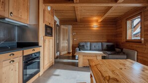 A wooden cabin interior with a kitchen, dining area, and a sofa.