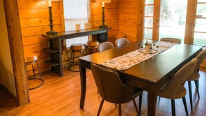 Ein Holzblockhaus-Interieur mit Esstisch, Stühlen und einer Bar mit Hockern.