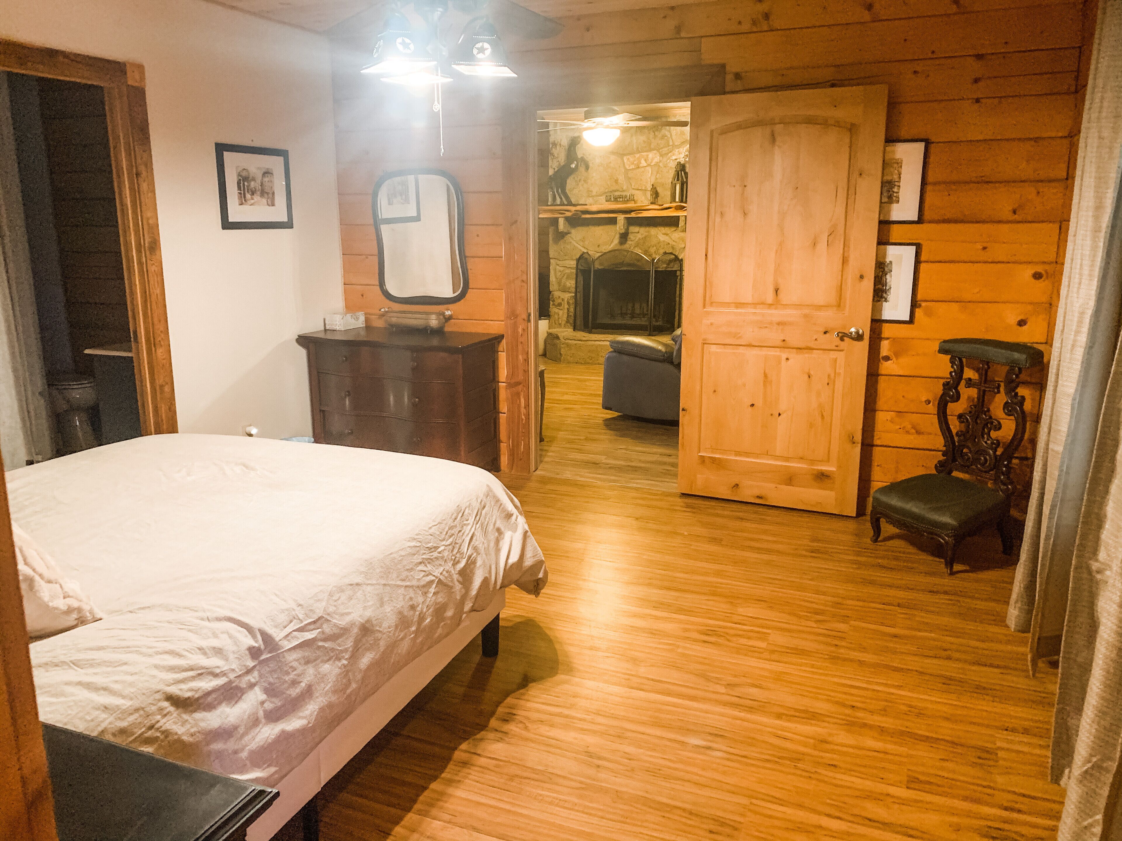 A wooden-paneled room with a bed, a dresser, a mirror, and a door leading to another room.