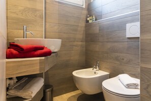 A modern bathroom with a wooden wall, a white sink, a bidet, and a toilet.