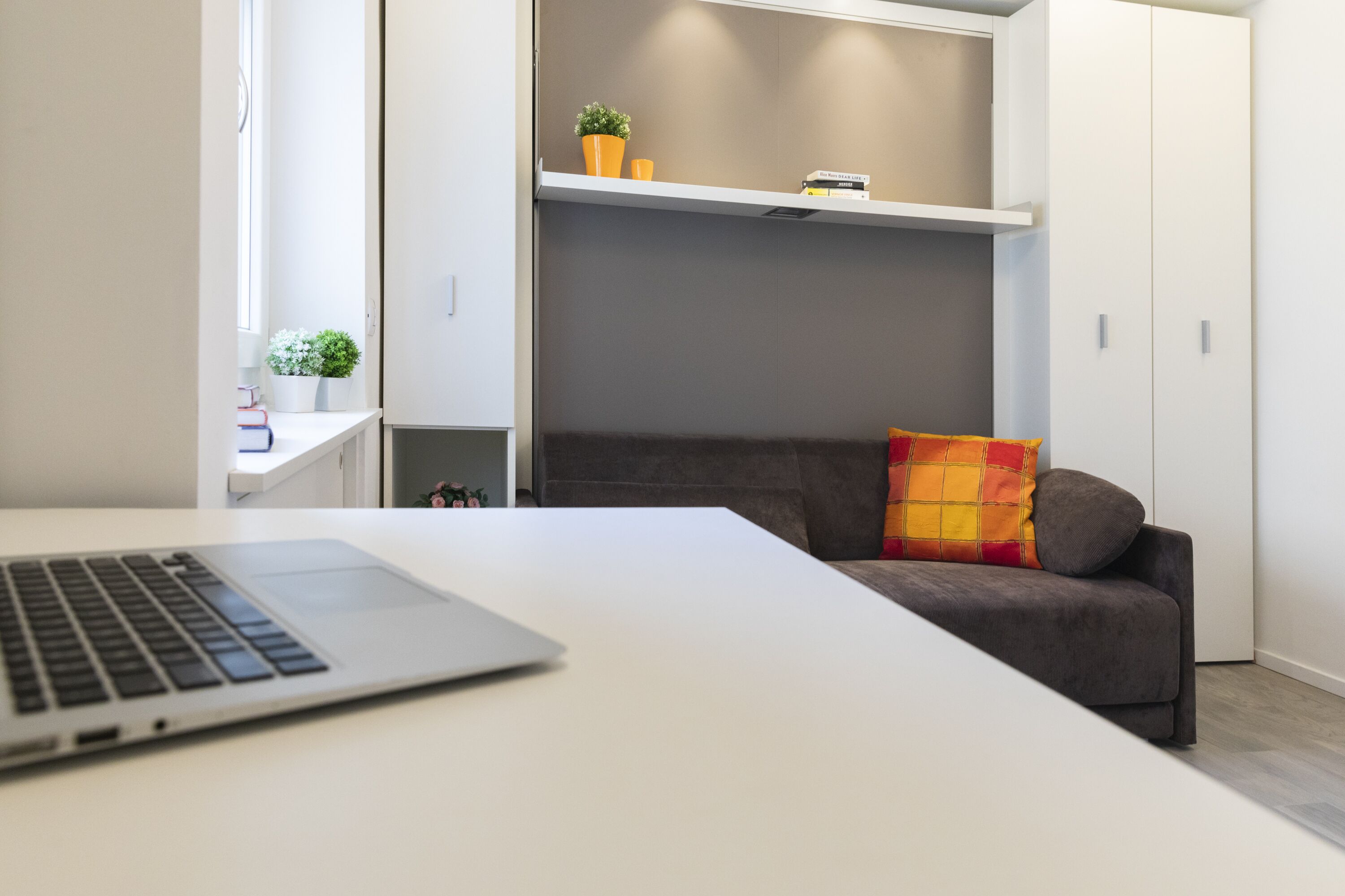 A modern room with a white desk, a grey sofa, and a shelving unit with decorative items.