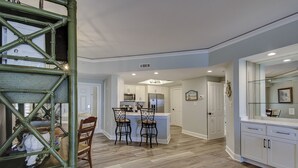 A modern kitchen with white cabinets, a central island with bar stools, and a dining area with a wooden table and chairs. - 5105 Hampton Place - Amazing Views (Hilton Head Island)
