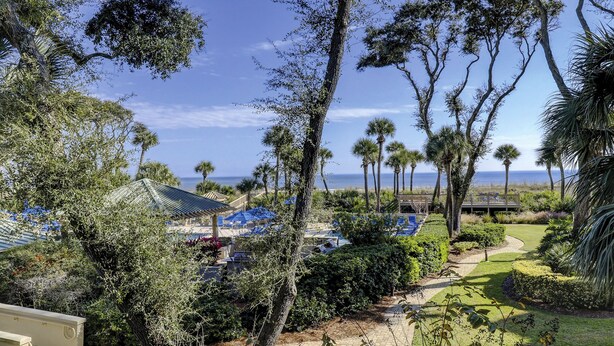 A resort with a pool area, palm trees, and a view of the ocean. - 5105 Hampton Place - Amazing Views (Hilton Head Island)