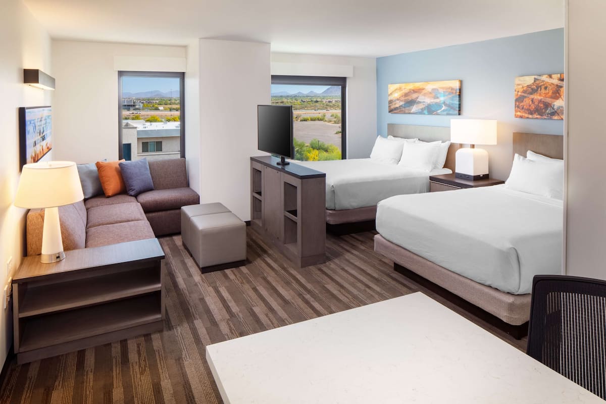 Una habitación de hotel con sofá, dos camas, televisión y escritorio.