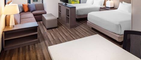 A hotel room with a sofa, two beds, a TV, and a desk.